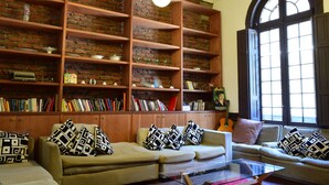 A cozy living room with a brick wall, wooden bookshelves, and two sofas with patterned cushions.