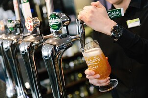 A person pouring beer from a tap labeled "Carlsberg" into a glass.