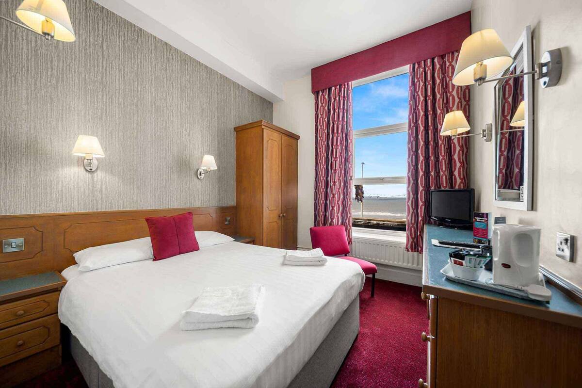 Une chambre d’hôtel avec un grand lit, un bureau avec une télévision et une fenêtre avec des rideaux.