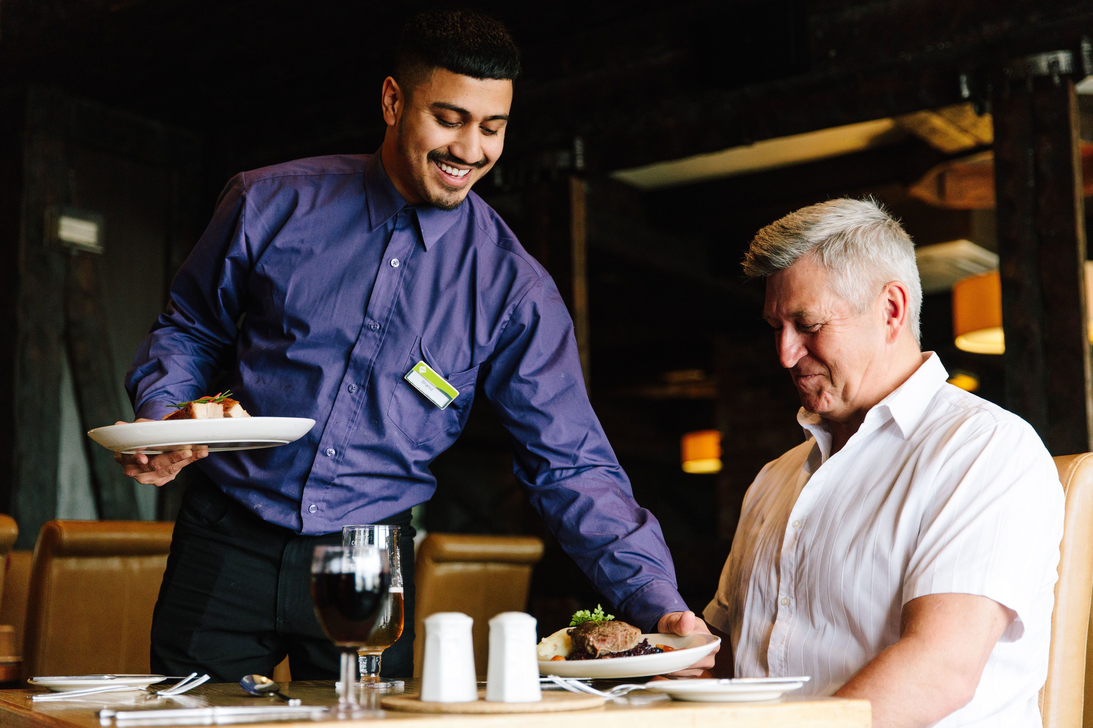 Een ober serveert een maaltijd aan een gast in een restaurant.