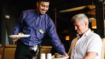Een ober serveert een maaltijd aan een gast in een restaurant.