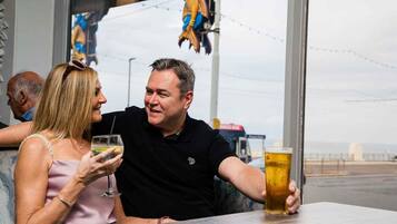 Twee personen zitten aan een tafel met drankjes, met uitzicht op een brug en water.