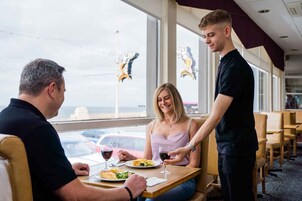 Een eetgedeelte met een tafel, stoelen en een ober die eten serveert.