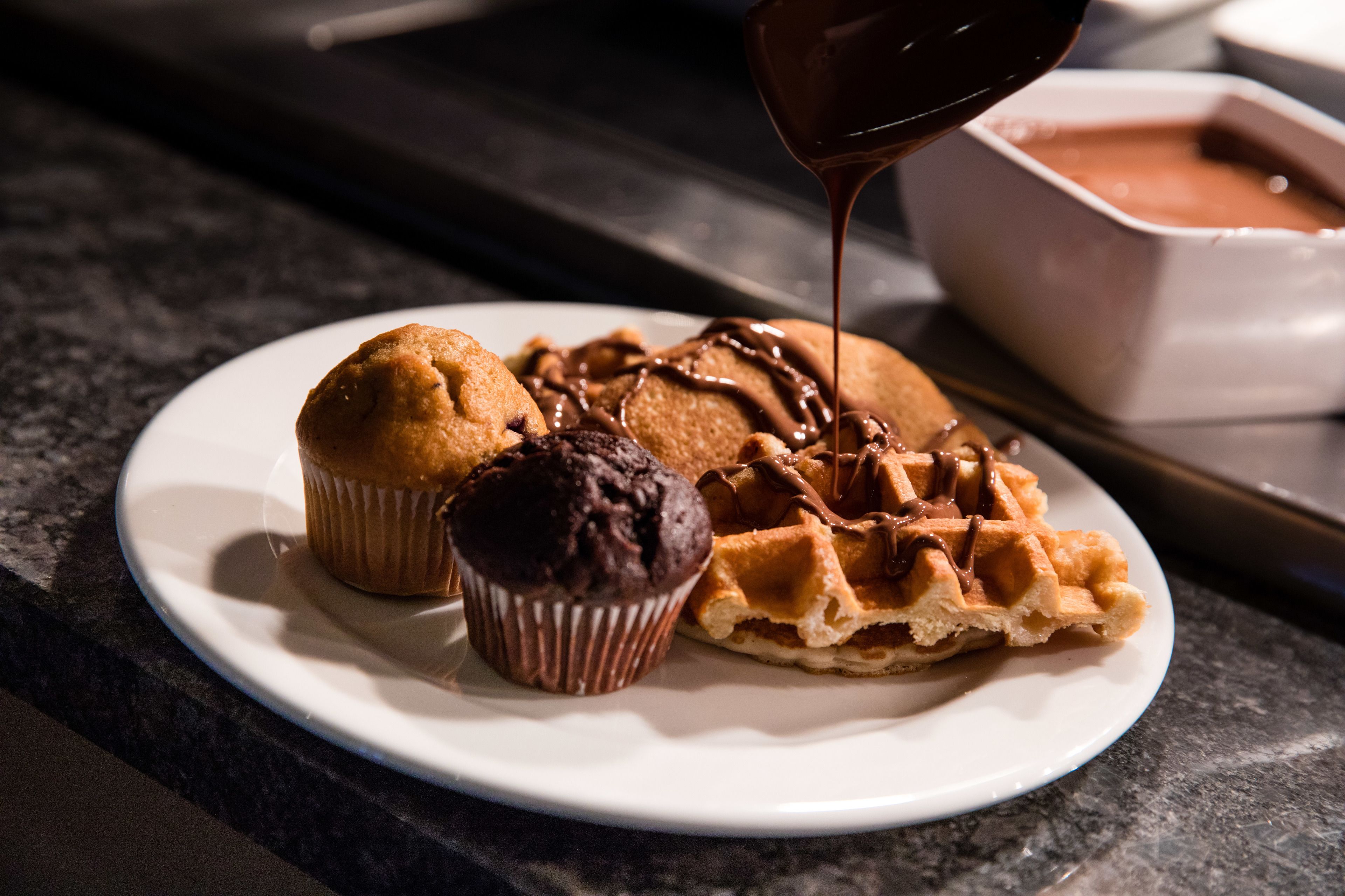A plate with a muffin, a chocolate cupcake, and a waffle topped with chocolate sauce.