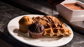 A plate with a muffin, a chocolate cupcake, and a waffle topped with chocolate sauce.