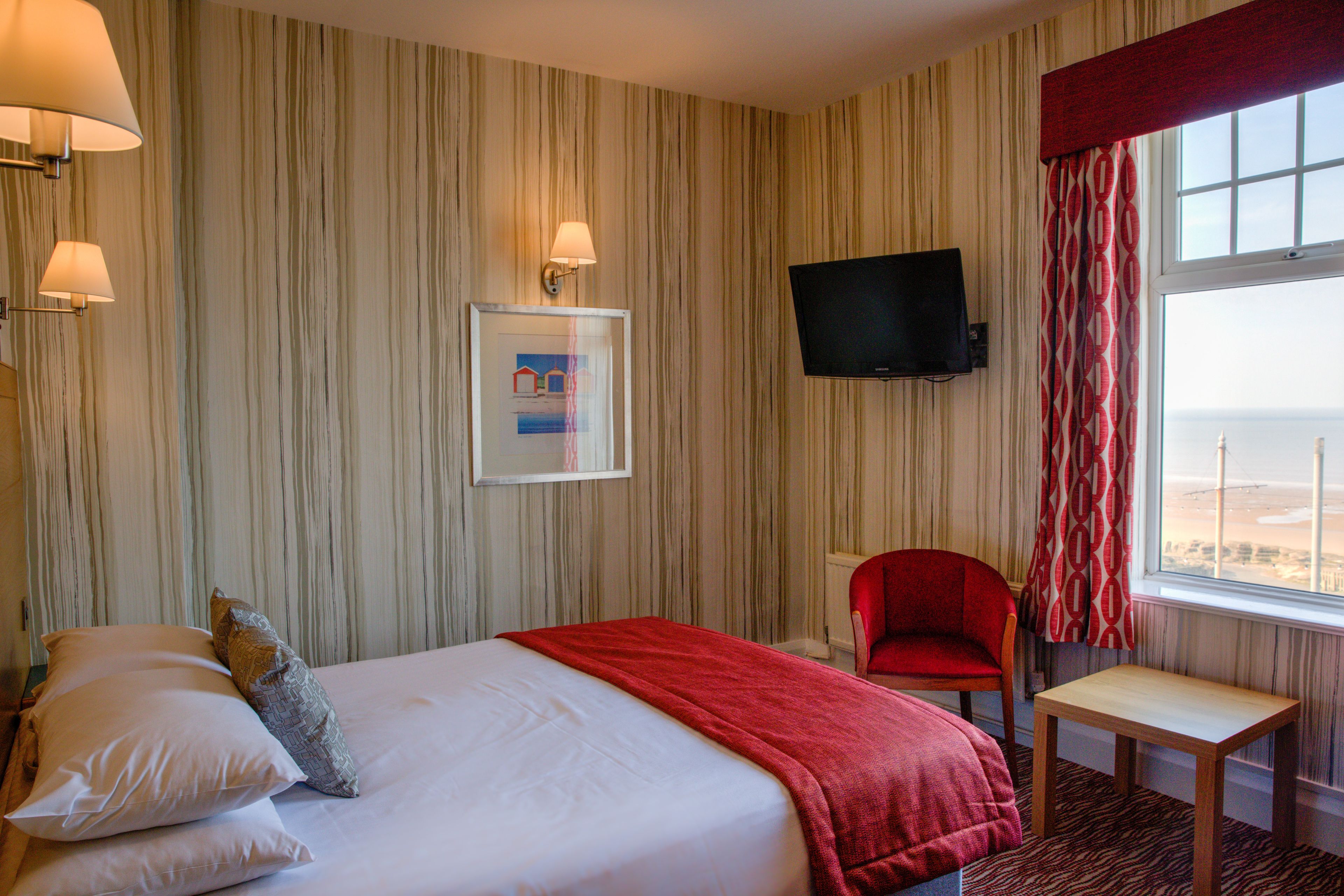 A hotel room with a bed, a desk, a chair, a TV, and a window with a view.