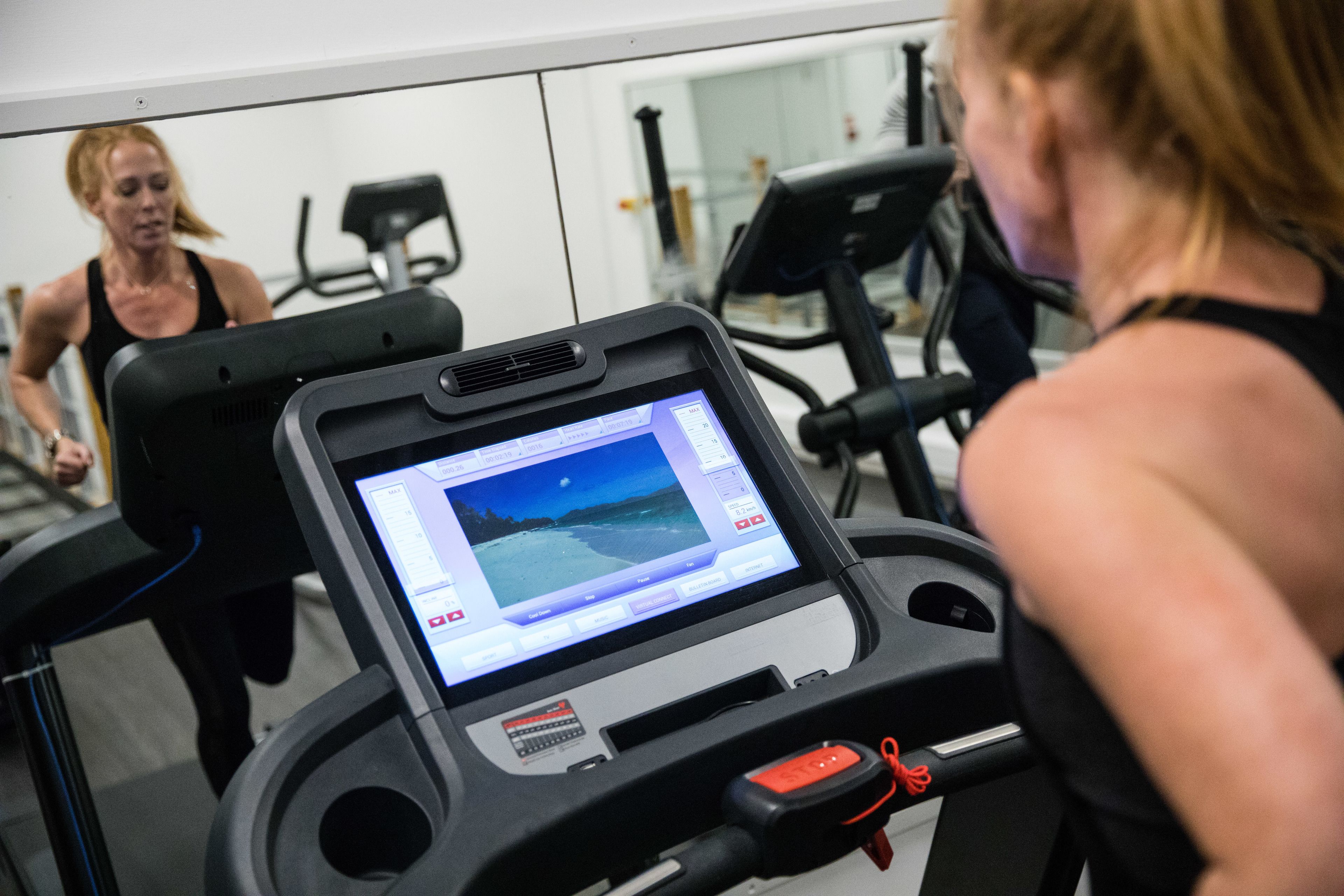 Una cinta de correr con pantalla digital, un espejo y equipo de ejercicio en un gimnasio.