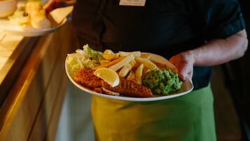 Una persona sostiene un plato con un filete de pescado, papas fritas y una salsa verde.