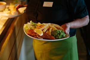 Una persona sostiene un plato con un filete de pescado, papas fritas y una salsa verde.