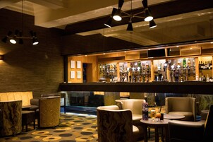 Een bar met zitplaatsen en diverse flessen en glazen op planken.