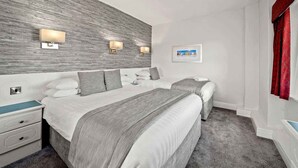 A hotel room with two beds, a wooden accent wall, bedside lamps, a nightstand, a dresser, and a framed picture on the wall.