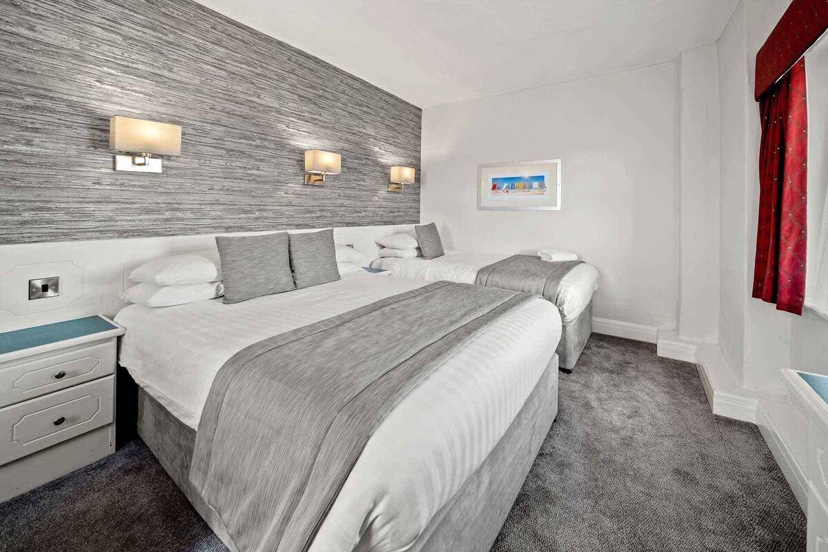 Habitación de hotel con dos camas, un cabecero de madera, lámparas de noche, mesitas de noche, cómoda y un cuadro enmarcado en la pared.