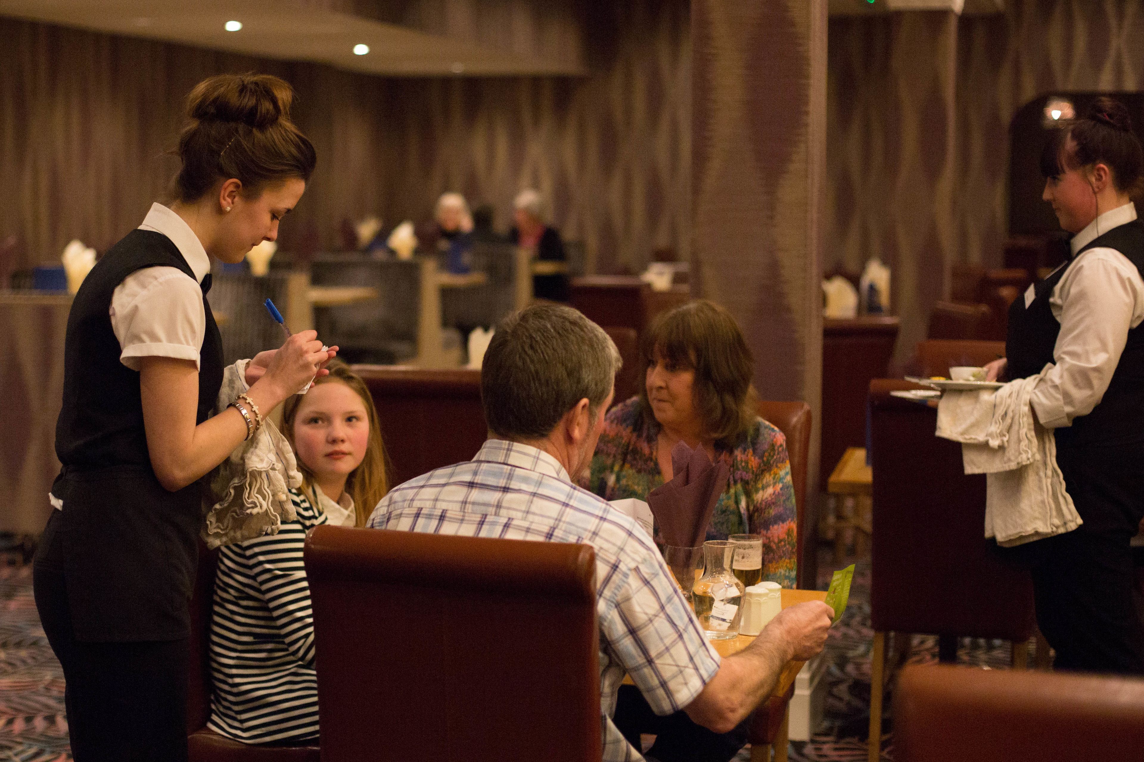 A restaurant setting with diners seated at tables, waitstaff attending to them.
