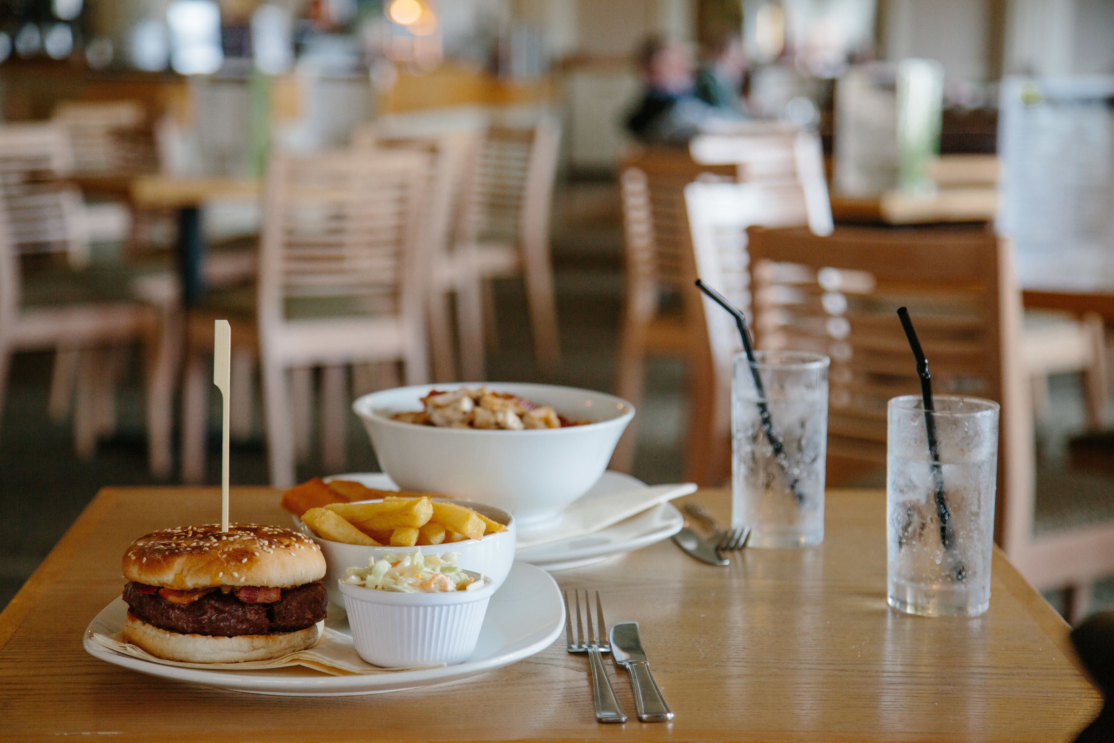 Una mesa de comedor con una hamburguesa, un bol de papas fritas y un vaso de té helado.