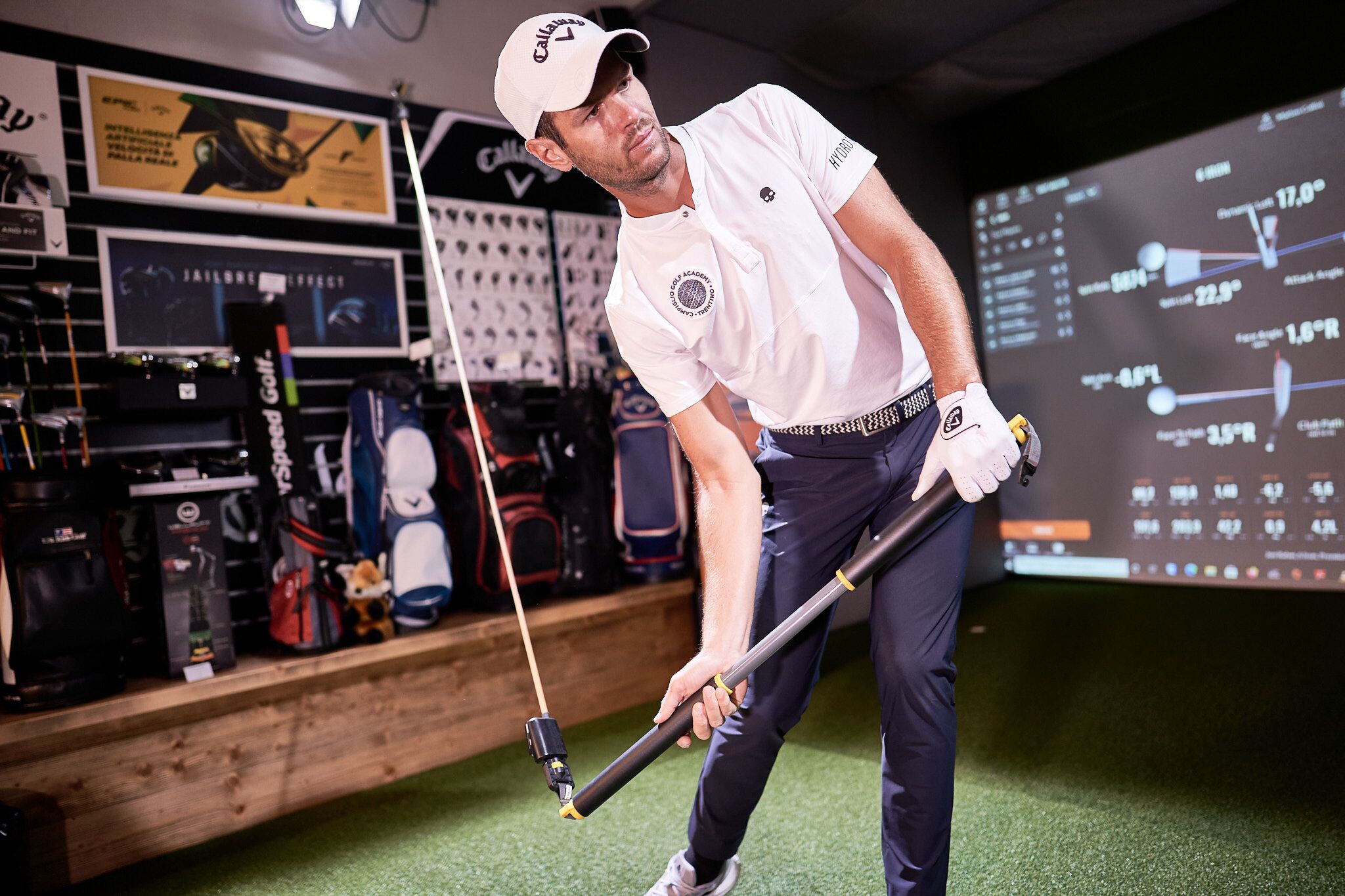 A man in a golf setting with a display of golf equipment and a digital screen showing golf statistics.