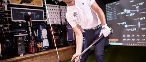 A man in a golf setting with a display of golf equipment and a digital screen showing golf statistics.