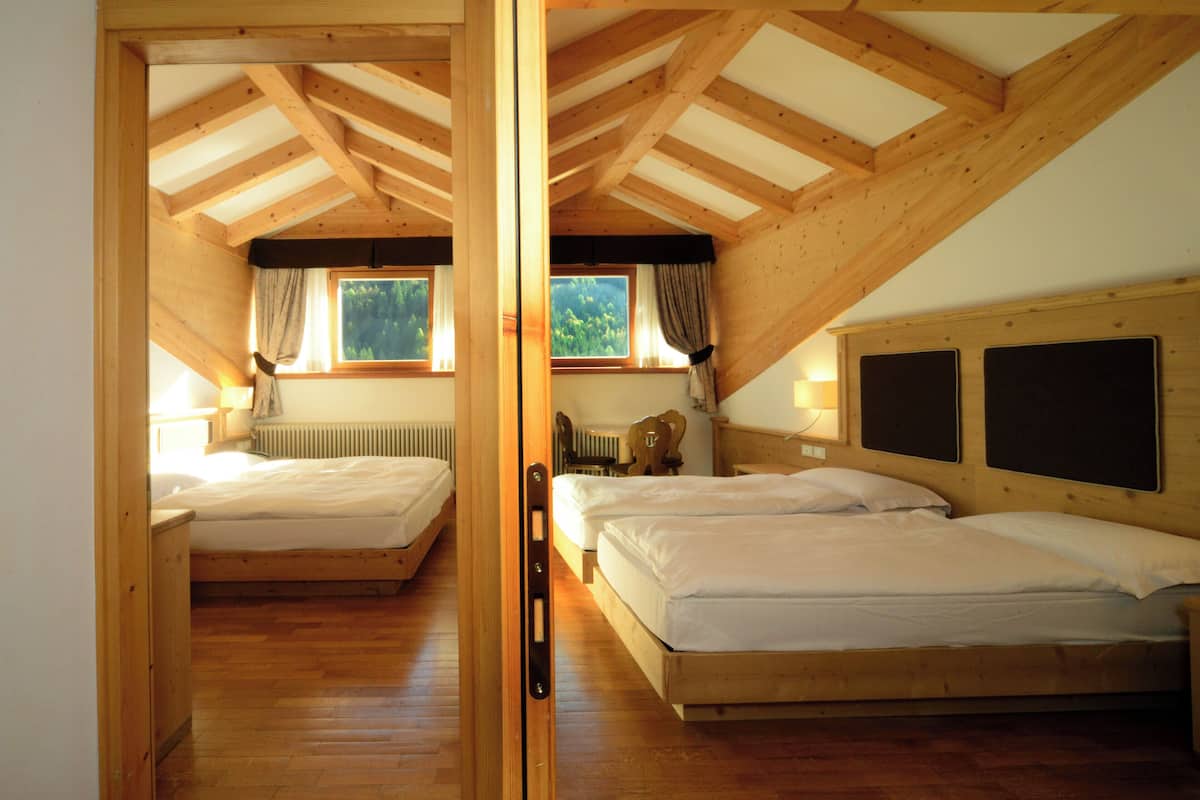A room with wooden beams, two beds, a window with curtains, and a radiator.