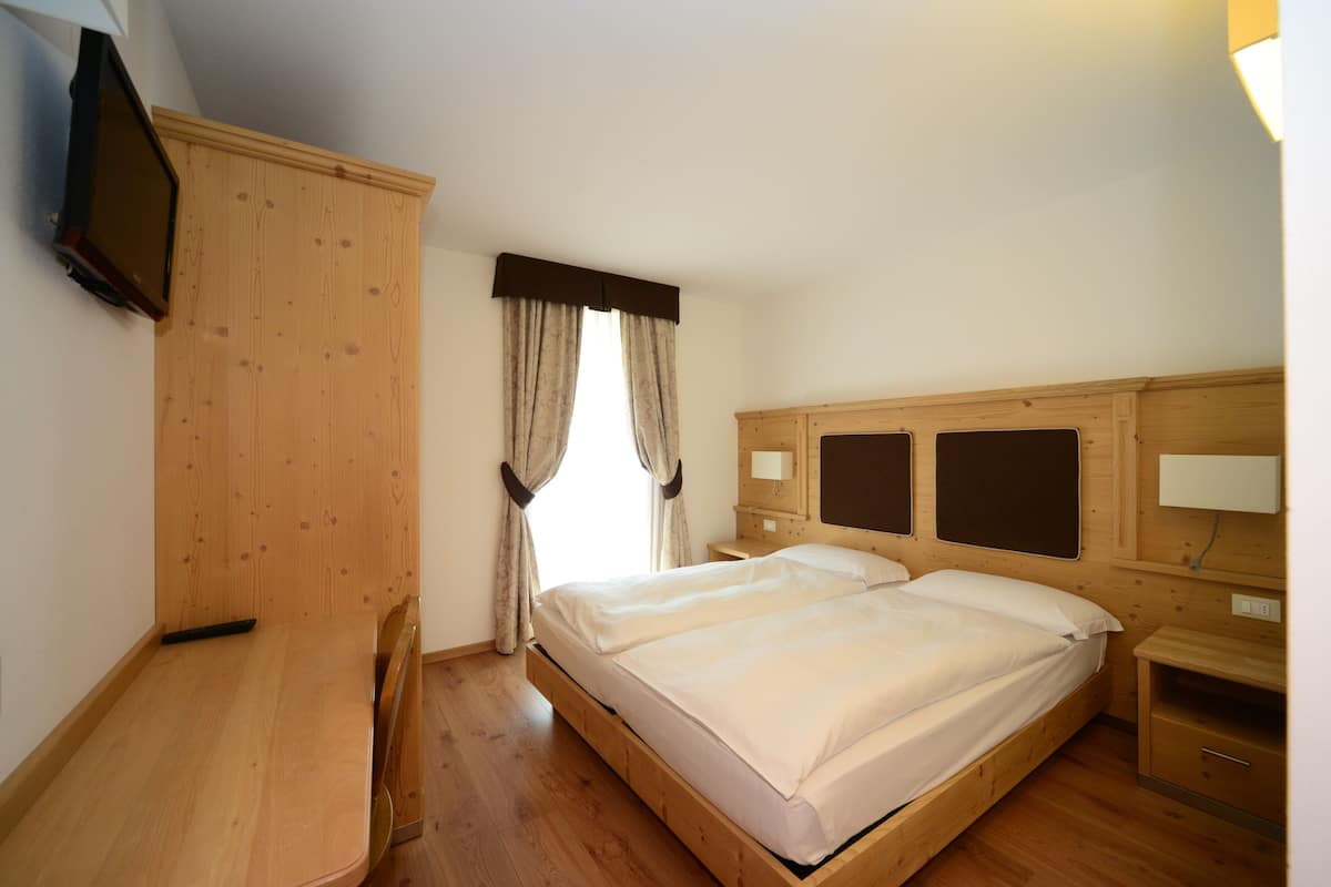 A bedroom with a wooden bed, a desk, and a TV mounted on the wall.