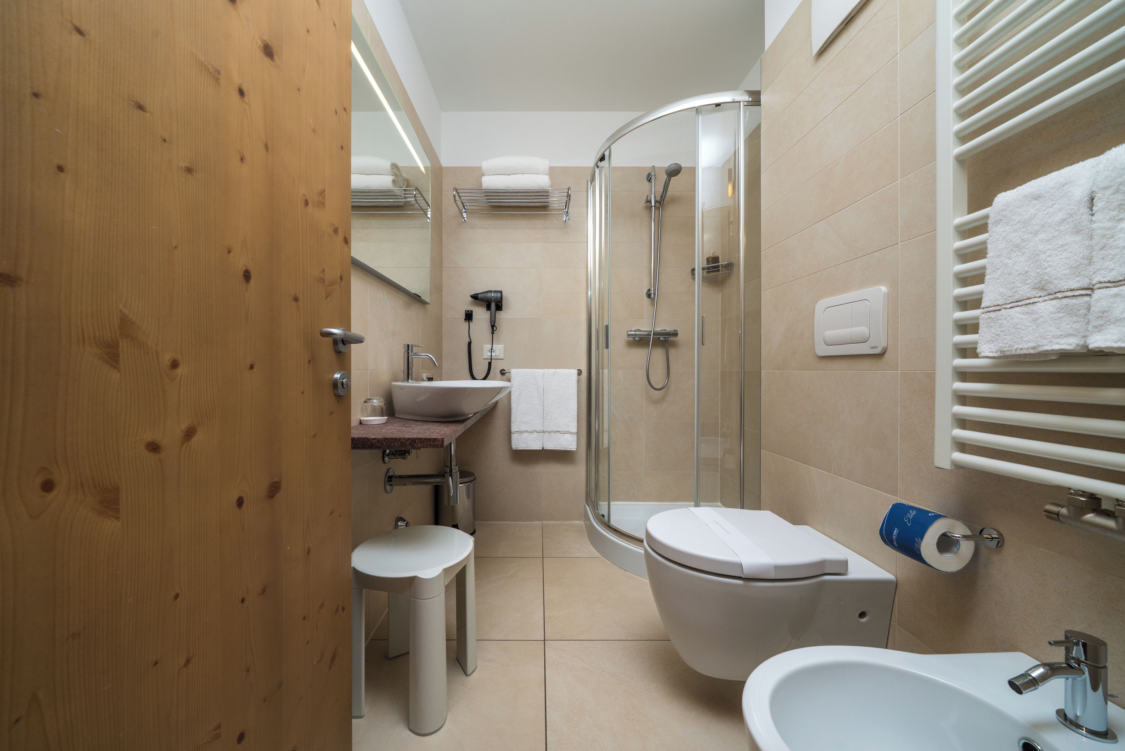 A modern bathroom with a shower, toilet, sink, and a wooden door.
