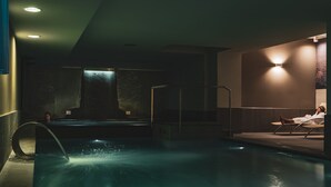 Piscina con fuente, una tumbona y un aplique de pared.