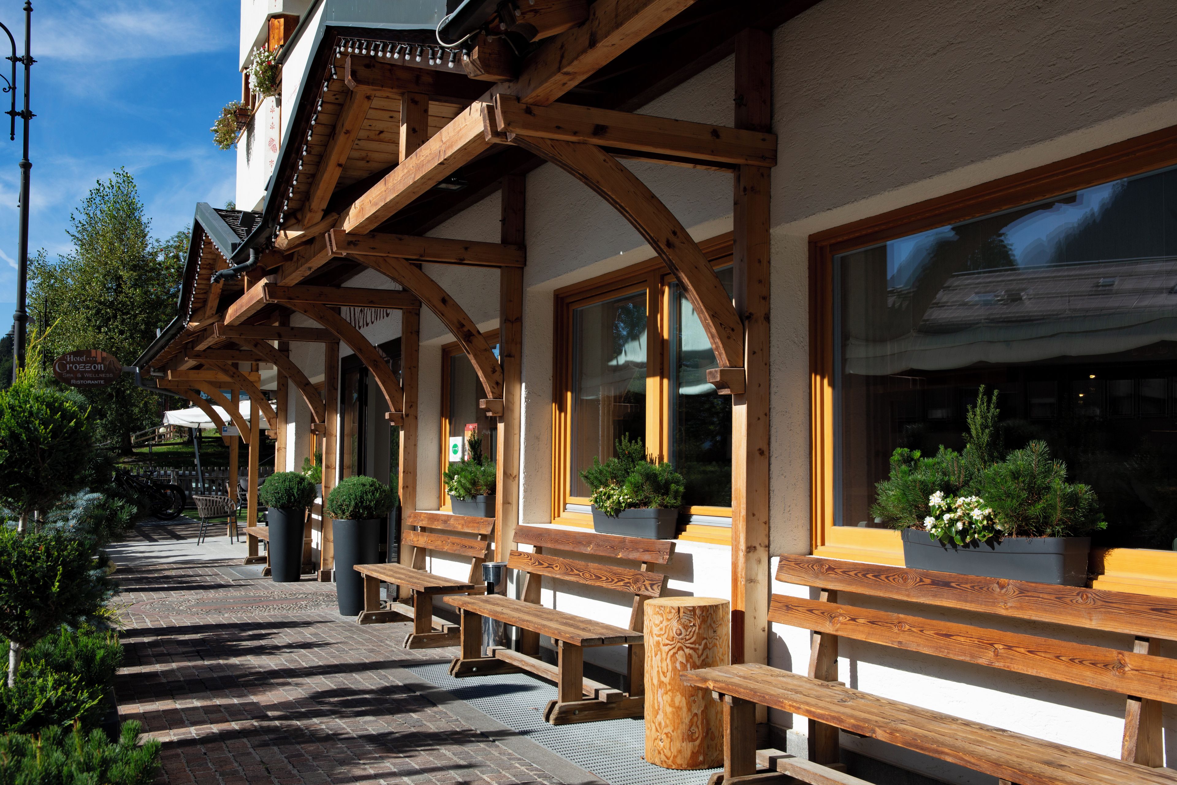 Un espace extérieur aménagé en bois, avec des bancs et des plantes en pot, un ciel dégagé et un bâtiment doté de grandes fenêtres.