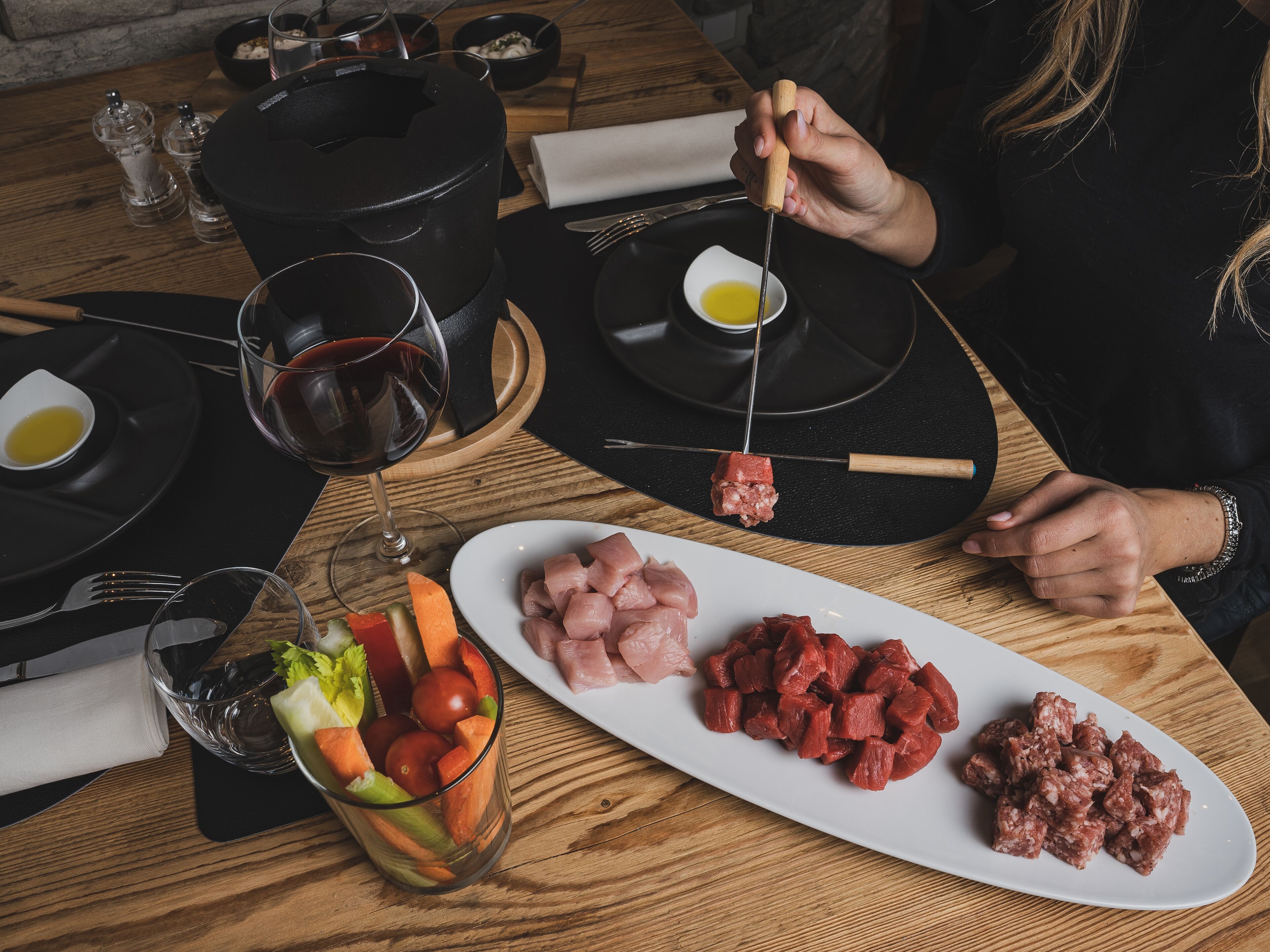 A dining table with a hot pot, a glass of red wine, and various dishes including meat and vegetables.