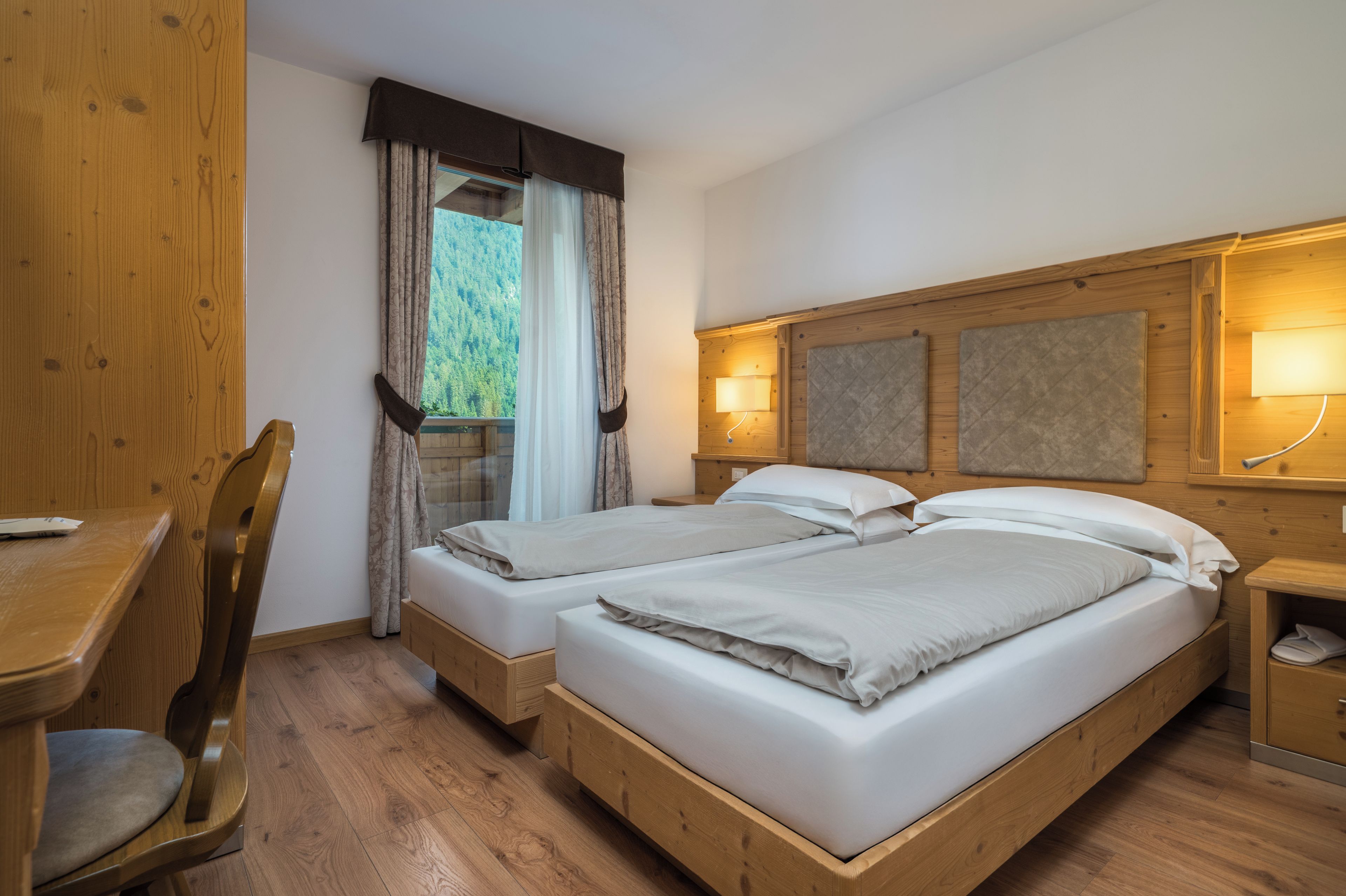 A double bed with a wooden headboard, a bedside table with a lamp, and a window with curtains.