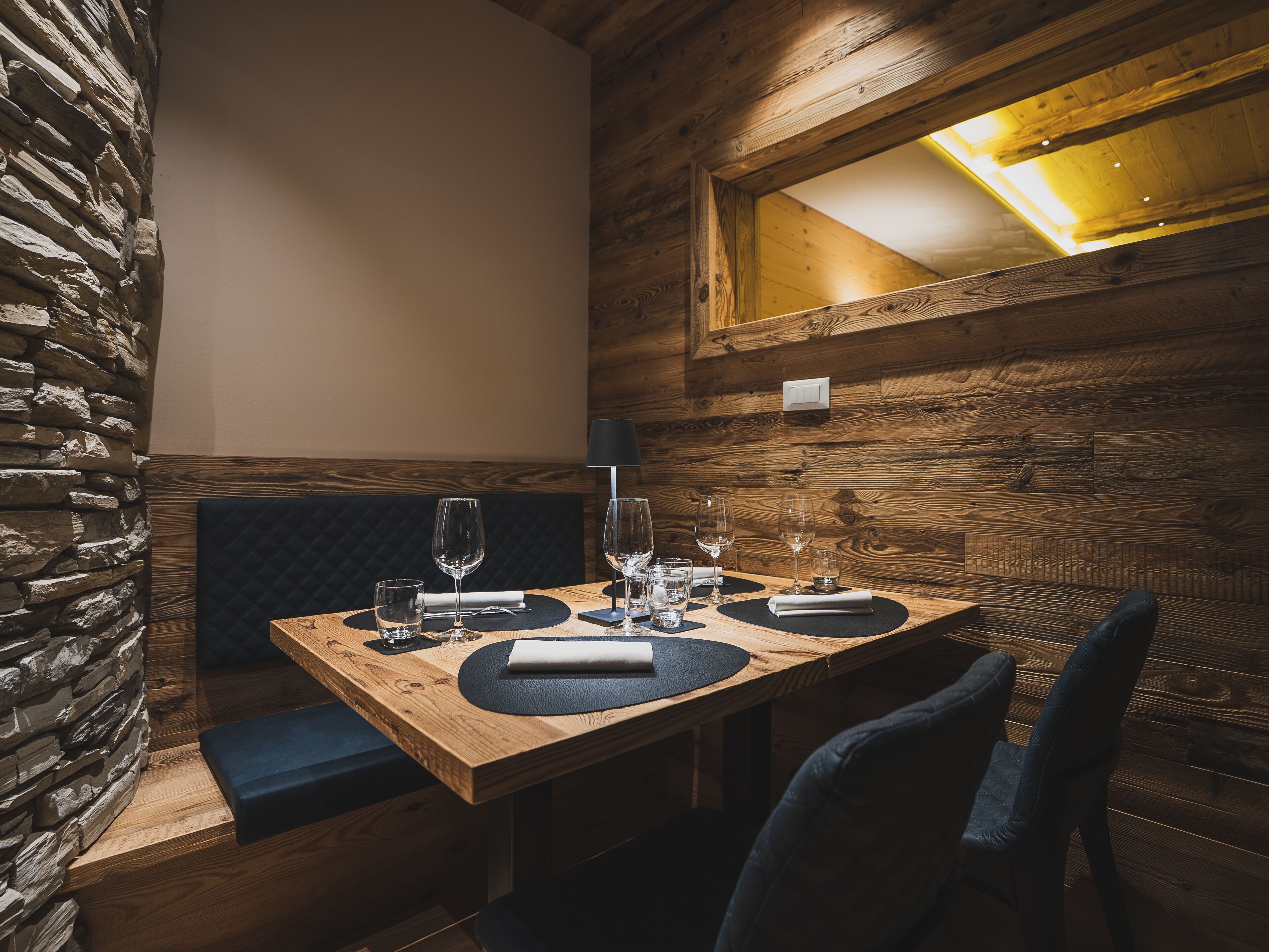 Un tavolo da pranzo in legno con una panca imbottita nera, una parete in pietra e un soffitto in legno con un lucernario.
