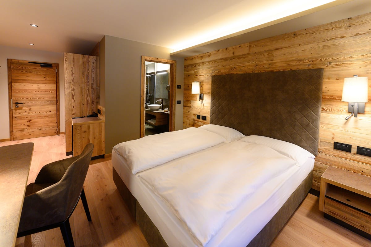 A bedroom with a double bed, wooden headboard, bedside tables, a desk with a chair, and a wooden wardrobe.