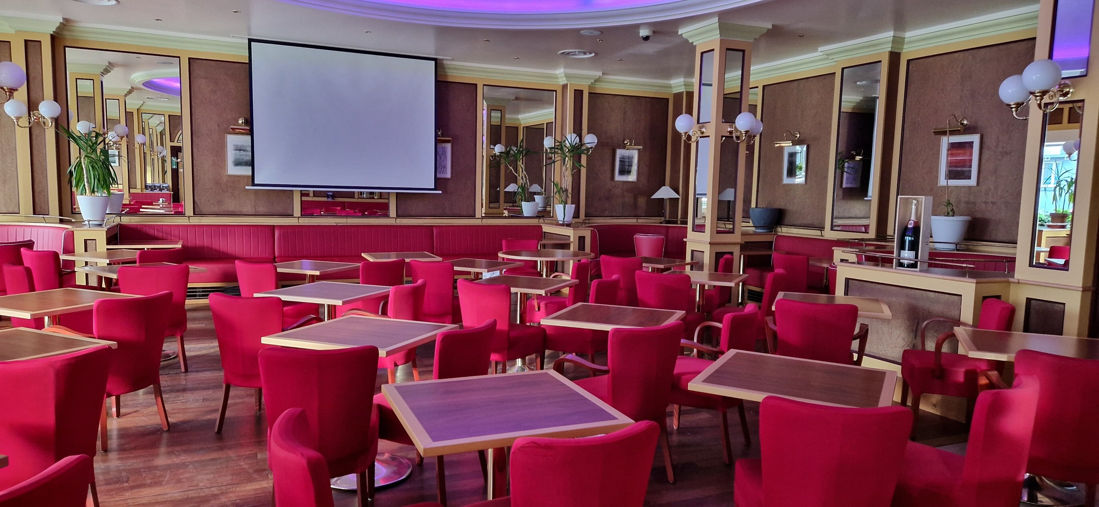 A restaurant with red seating, a large screen, and mirrors on the walls.