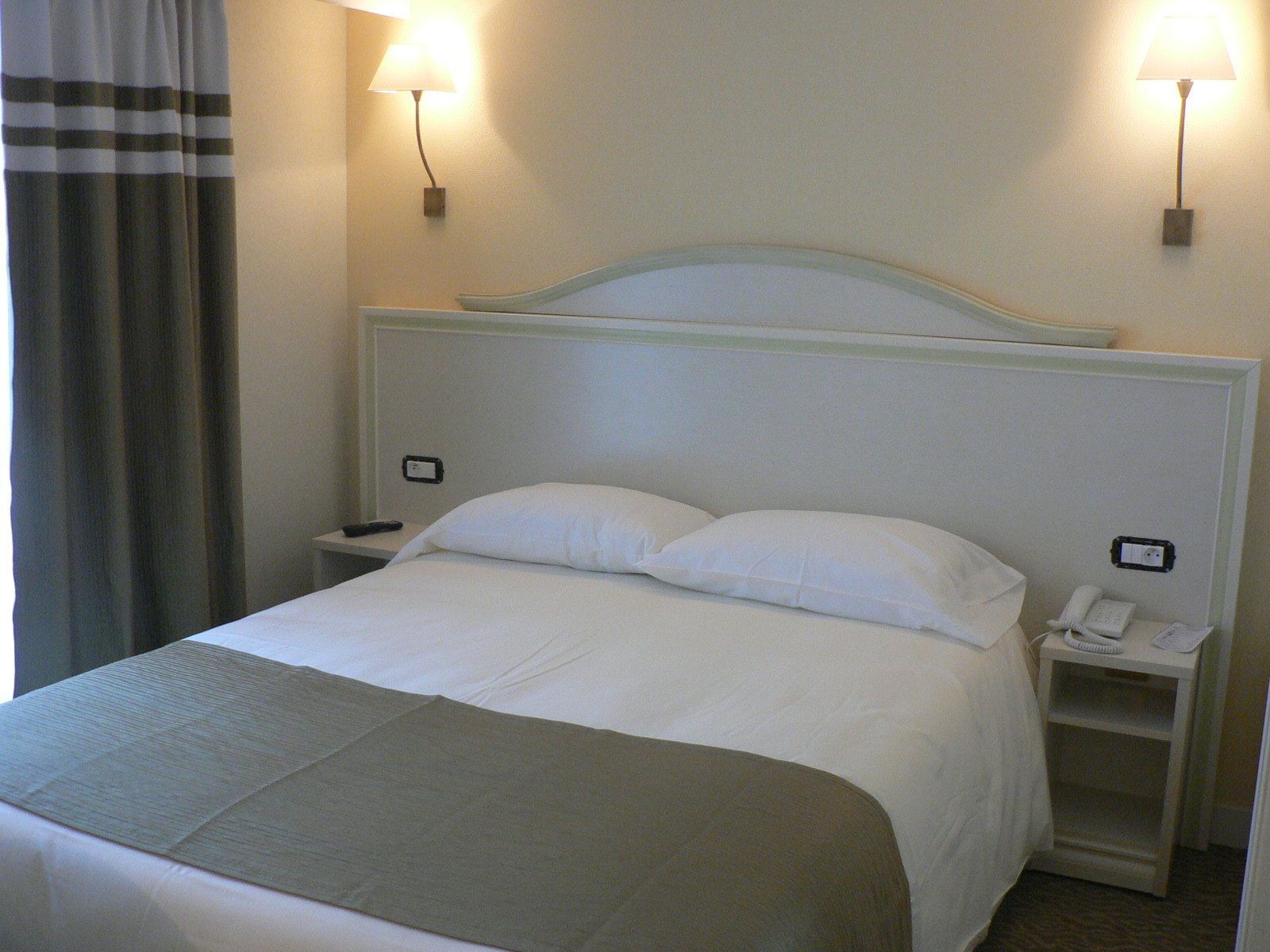 Una habitación de hotel con una cama, dos mesitas de noche, una lámpara y un teléfono.