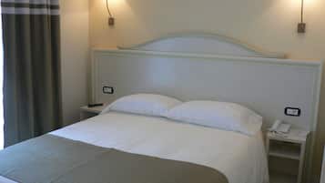 Una habitación de hotel con una cama, dos mesitas de noche, una lámpara y un teléfono.