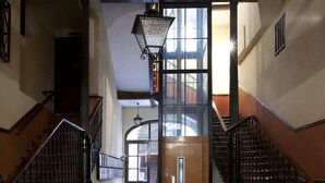 Un pasillo con una puerta de madera al fondo, flanqueado por dos escaleras con barandillas negras.