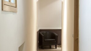 Un pasillo estrecho con suelo de baldosas, una silla negra y una puerta de madera.
