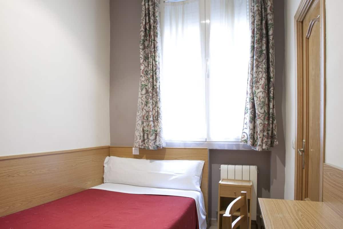A hotel room with a single bed, a small table, and a chair.