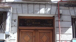 Una amplia puerta doble de madera con tallas complejas, ubicada en un edificio de piedra con una reja metálica a la izquierda.