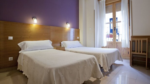 Habitación de hotel con dos camas, cabeceros de madera y una ventana con cortinas.