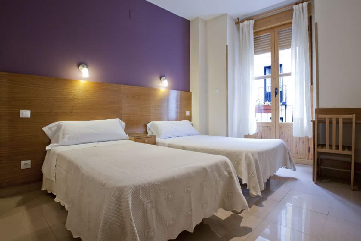 A hotel room with two beds, wooden headboards, and a window with curtains.