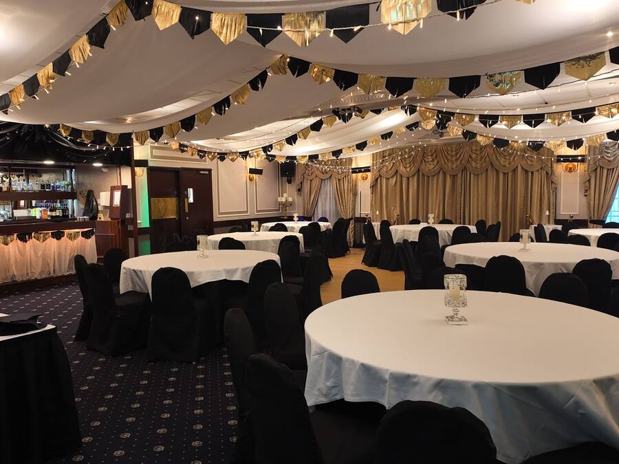 A banquet hall with round tables, black chairs, and a bar area.
