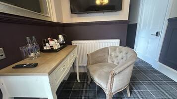 A room with a white desk, a television mounted on the wall, a radiator, and a tufted armchair.