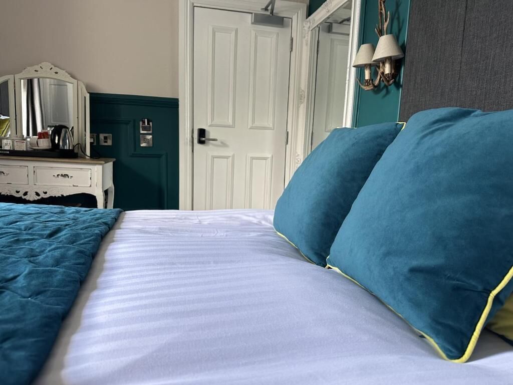 A bed with blue pillows, a white dresser, and a door in the background.