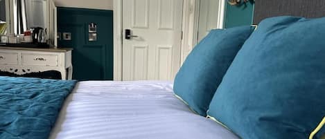 Ein Bett mit blauen Kissen, eine weiße Kommode und eine Tür im Hintergrund.