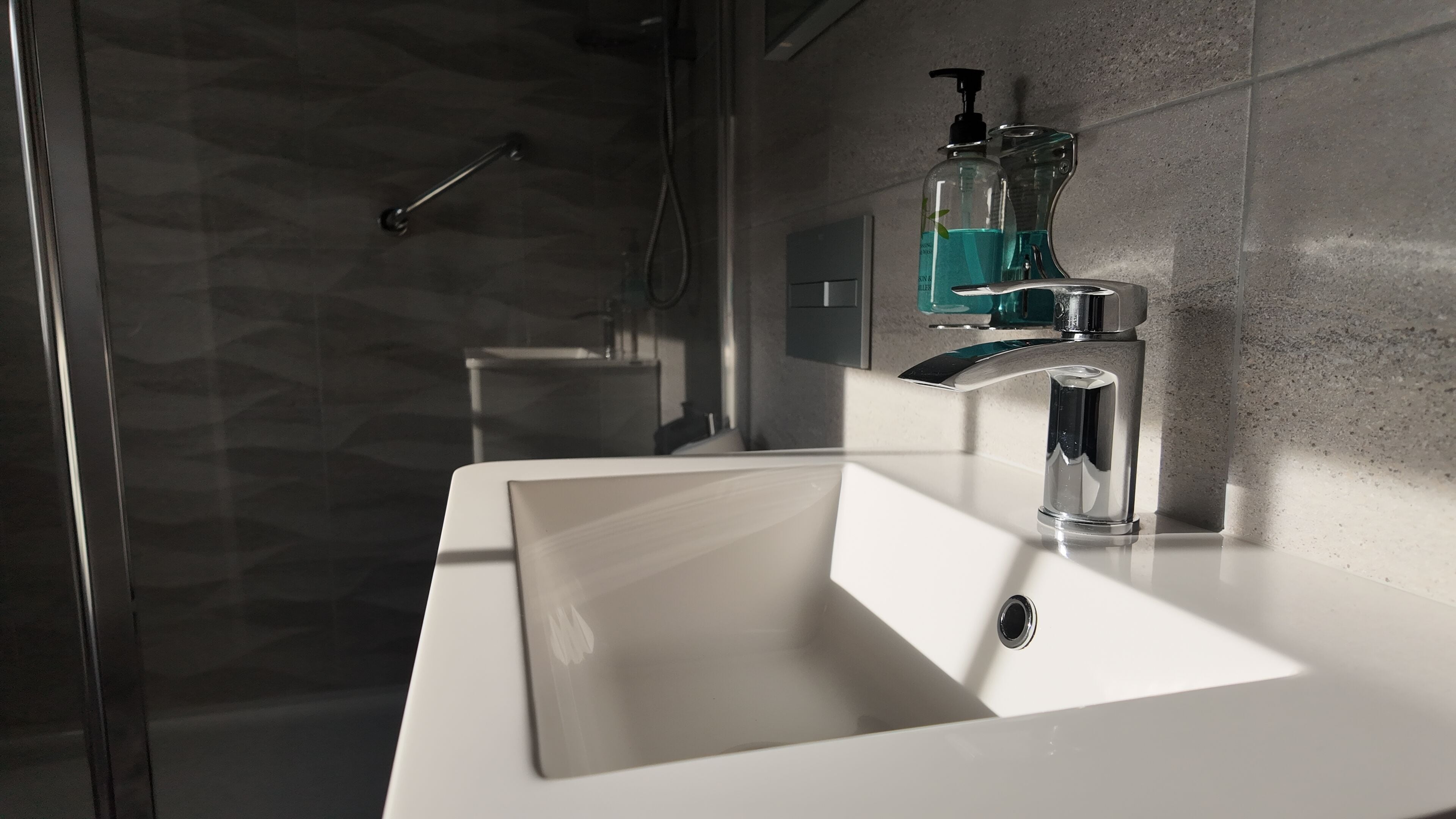 A bathroom with a white sink, a chrome faucet, and a glass soap dispenser.