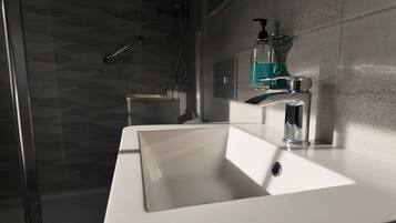 A bathroom with a white sink, a chrome faucet, and a glass soap dispenser.