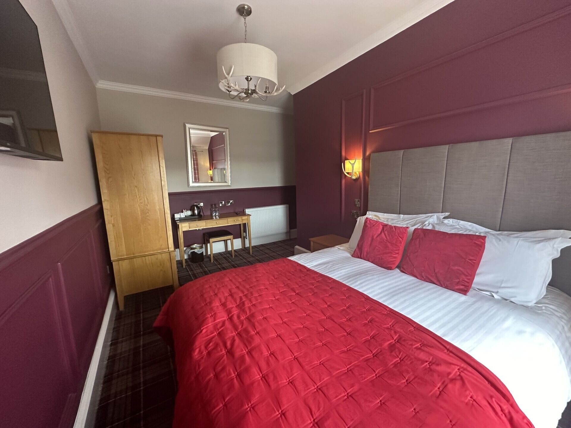 Ein Hotelzimmer mit einem großen Bett, einem Holzschrank, einem Schreibtisch mit Stuhl, einem Spiegel und einer Chandelier.