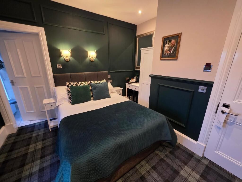 Una habitación de hotel con una cama, una mesita de noche, una lámpara de pared y una puerta.
