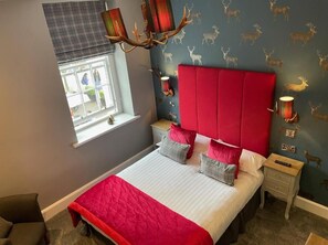 A bedroom with a bed, a nightstand, a window with blinds, and a wall with deer decals. - The Original Rosslyn Inn (Roslin)