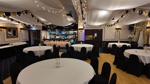 A banquet hall with round tables, black chairs, and white tablecloths. - The Original Rosslyn Inn (Roslin)