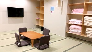 A room with tatami flooring, a low table, four chairs, and shelves with folded towels. - Golden Time Takamatsu (Takamatsu)