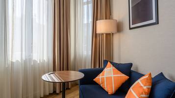 A room with a blue sofa, two orange pillows, a round table, and a lamp.